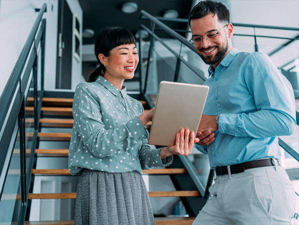 Shot of two colleagues using a digital tablet while walking down stairs in a modern office