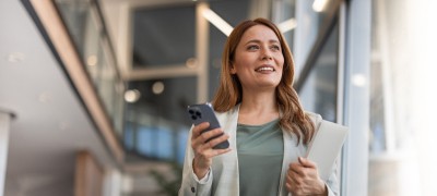 A woman smiling and holding a smartphone in her hand.