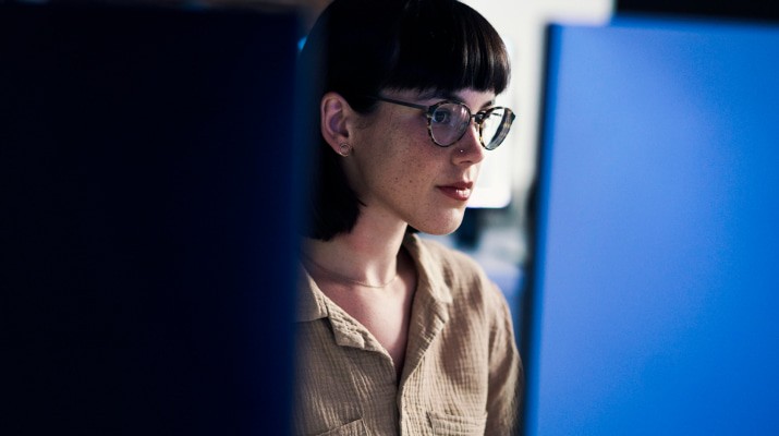 A woman with glasses looking at her computer in front of her.